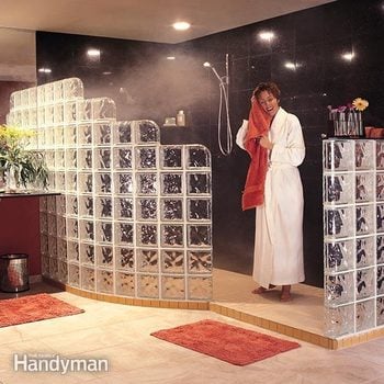 Woman in a robe dries her hair after walking out of a glass block shower